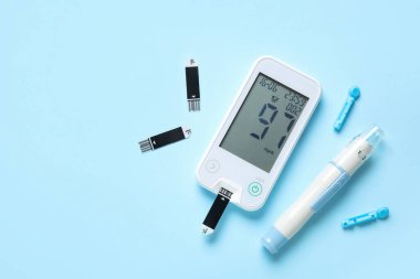 Glukometre, tükenmez kalem, tek kullanımlık iğneler ve mavi arka planda test şeritleri. Diyabet kavramı
