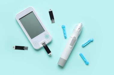 Glukometre, tükenmez kalem, tek kullanımlık iğneler ve turkuaz arka planda test şeritleri. Diyabet kavramı