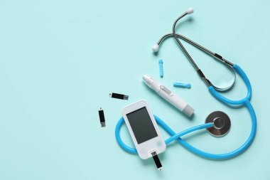 Glukometre, tükenmez kalem, steteskop ve turkuaz arka planda test şeritleri. Diyabet kavramı