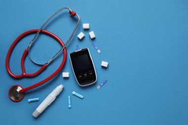 Glukometre, tükenmez kalem, şeker, steteskop ve mavi arka planda test şeritleri. Diyabet kavramı