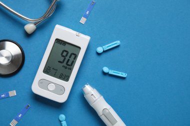 Glukometre, tükenmez kalem, tek kullanımlık iğneler ve mavi arka planda test şeritleri. Diyabet kavramı