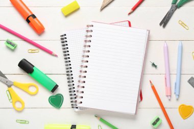 Beyaz ahşap zemin üzerine boş defterler ve kırtasiye malzemeleri içeren kompozisyon, yakın plan