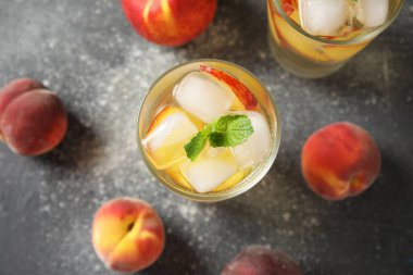 Şeftali dilimli bir bardak içecek, buz küpleri ve gri grunge arka planda nane yaprakları.