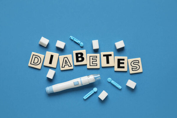 Слово Диабет с ручкой ланцета, сахар и одноразовые иглы на синем фоне. Концепция диабета