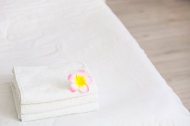 Otel odasındaki yatağın üzerinde pembe Plumeria çiçeği olan bir yığın temiz havlu.