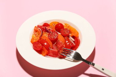 Pembe arka planda kırmızı soğanlı taze domates salatası, yakın plan.