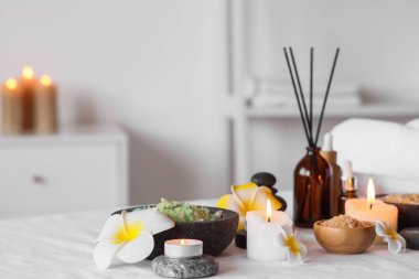 Plumeria çiçekli beyaz kanepe, spa taşları, kamış ayırıcı ve banyoda yanan mumlar, yakın çekim.