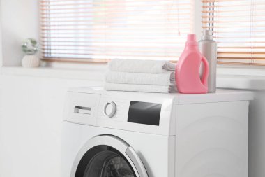 Çamaşır odasında temiz havlular ve şişe deterjan olan çamaşır makinesi, yakın plan.
