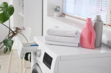 Çamaşır odasında temiz havlular ve şişe deterjan olan çamaşır makinesi, yakın plan.