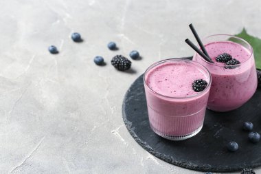 Gri arkaplanda taze böğürtlen suyu ve yabanmersini bardakları