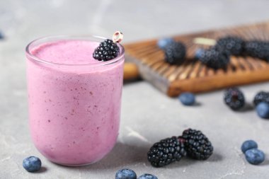 Gri arkaplanda bir bardak taze böğürtlen suyu ve yabanmersini.