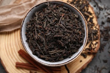 Siyah çay yapraklı kase ve koyu arkaplanda tarçın.