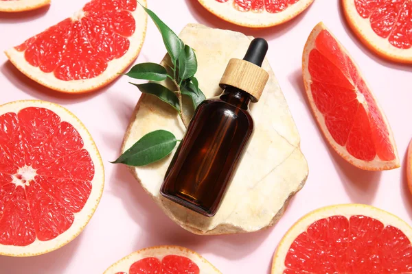 Bir şişe kozmetik ürünü, pembe arka planda greyfurt ve taş dilimleri, yakın plan.
