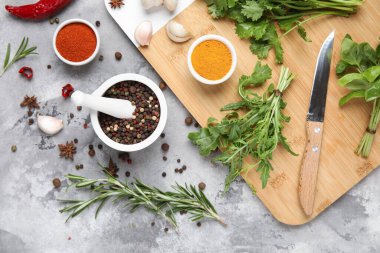 Ahşap kesim tahtasıyla kompozisyon, gri grunge arka planda otlar ve baharatlar, yakın plan