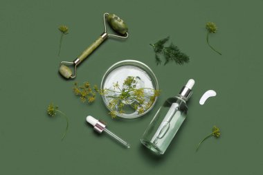 Petri kabı, yüz masajı aracı ve yeşil arka planda bir şişe dereotlu kozmetik ürünü, yakın plan