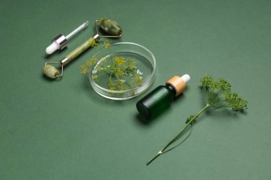 Petri kabı, yüz masajı aracı ve yeşil arka planda bir şişe dereotlu kozmetik ürünü, yakın plan