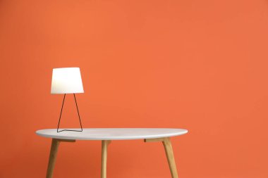 Turuncu duvarın yanında parlayan lamba olan kahve masası.