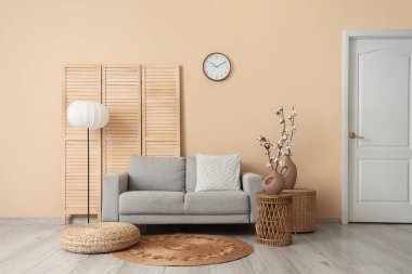 Gri kanepe, puf, hasır masalar ve oturma odasının içinde pamuk çiçekli vazolar.