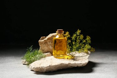 Üzerinde dereotu tohumu olan taşlar, siyah arka plana karşı gri masanın üzerinde gerekli yağ.