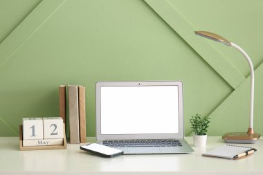 Modern dizüstü bilgisayar, cep telefonu, kitaplar ve takvim renkli duvarın yanındaki ışık masasında.