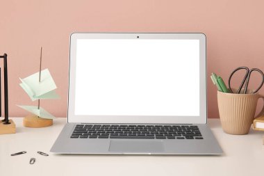 Modern dizüstü bilgisayar ve renkli duvarın yanındaki aydınlatma masasında farklı kırtasiye malzemeleri.