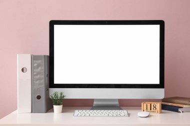 Modern bilgisayar monitörü, klavye, fare, takvim ve kırtasiye renkli duvarın yanındaki masada.