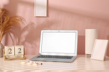 Modern dizüstü bilgisayar, takvim, lamba ve boş resim çerçevesi renk duvarının yanında.