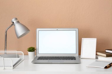 Modern dizüstü bilgisayar, boş çerçeve, lamba ve kırtasiye renkli duvarın yanındaki masada.