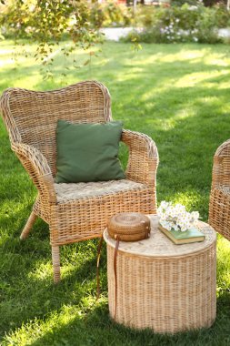 Rahat hasır koltuklar, papatya çiçekleri, kitap ve çanta parkta, açık havada kahve masasında.