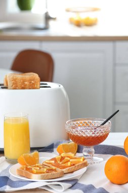 Lezzetli portakal reçelli tost tabağı, bir bardak meyve suyu ve mutfak masasında modern tost makinesi.