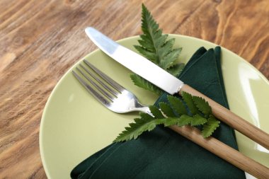 Ahşap masa üzerinde çatal bıçak ve eğrelti otu yaprakları olan güzel bir masa.