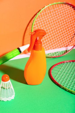 Bir şişe güneş kremi, badminton raketleri ve renkli arka planda mekik siki.