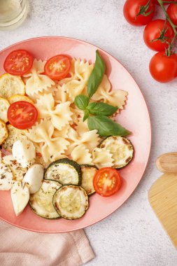 Beyaz arka planda domatesli ve fesleğenli lezzetli makarna salatası.