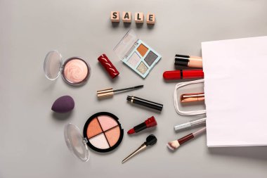 Makyaj malzemeli alışveriş çantası ve gri arka planda metin satışı