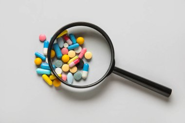 Gri arka planda farklı haplar içeren büyüteç