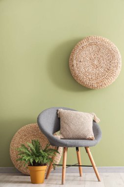 Oturma odasının içinde yeşil duvarın yanında koltuk, yastık ve çiçek var.