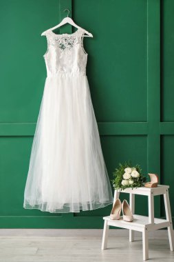 Güzel gelinlik yeşil duvarda yüzük kutusu, düğün ayakkabıları ve beyaz tahta merdiven üzerinde gelin buketi.