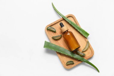 Ahşap tepsi, taze aloe yaprakları ve arka planda gerekli yağ şişesi.