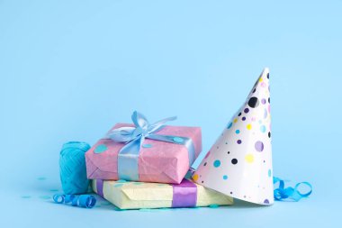 Hediye kutularıyla parti şapkası ve mavi arka planda konfeti.