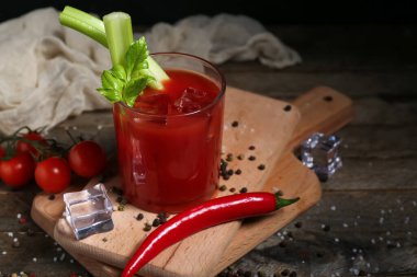 Bir bardak Bloody Mary kokteyli, kereviz, kırmızı biber ve ahşap masada biber.