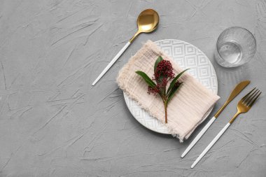 Altın çatal bıçak takımı ve gri arka planda skimmia japonica bitkisi olan güzel bir masa.