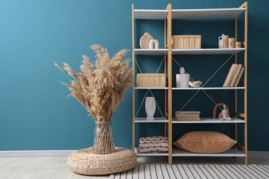 Süslü dekorlu kitaplık ve mavi duvarın yanında otlar.