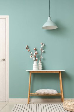 Oturma odasındaki yeşil duvarın yanındaki masada pamuk çiçekli vazolar, yakın plan.