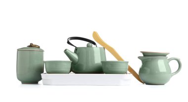 Çaydanlık, bardak, sürahi ve bambu maşayla beyaz arka planda tahta tepsi.