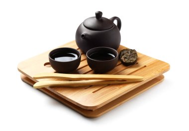 Çaydanlık tepsisi, çay fincanları, beyaz arka planda kuru ütülenmiş puer yaprakları ve bambu maşası.