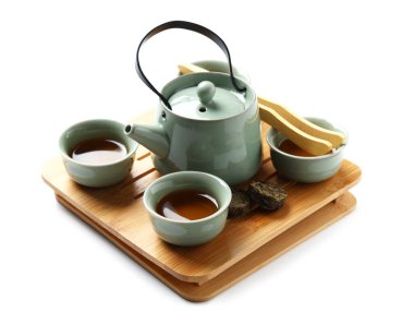 Çaydanlık tepsisi, çay fincanları, beyaz arka planda kuru ütülenmiş puer yaprakları ve bambu maşası.