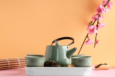 Çaydanlık tepsisi, çay fincanları, kuru ütülü puer yaprakları, bambu hasırı ve arkaplanda erik çiçeği dalı