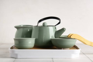 Çaydanlık tepsisi, çay fincanı, sürahi ve bambu maşası beyaz fayans üzerinde.