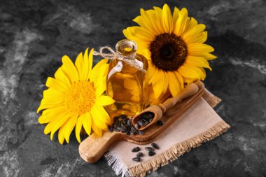 Tahta kesme tahtası, bir şişe ayçiçeği yağı ve siyah grunge arka planda bir kepçe tohum, yakın plan.