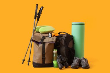 Sarı arka planda yürüyüş direkleri, sırt çantaları ve yürüyüş ekipmanları